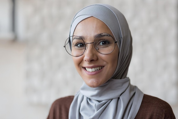 Close-up foto portret van jonge lachende moslimvrouw in glazen en grijze hijab arabische vrouw thuis