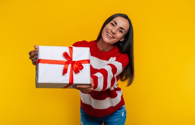 Close-up foto van aantrekkelijke lachende gelukkig opgewonden jonge brunette vrouw met geschenkdoos in handen geïsoleerd op gele achtergrond