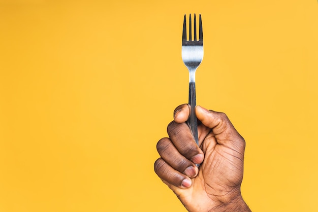 Close-up foto van Afro-Amerikaanse mannelijke hand met een vork geïsoleerd op gele achtergrond.