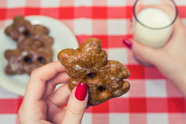 Close-up foto van de handen van de vrouw met koekje en glas melk over geruit tafelkleed