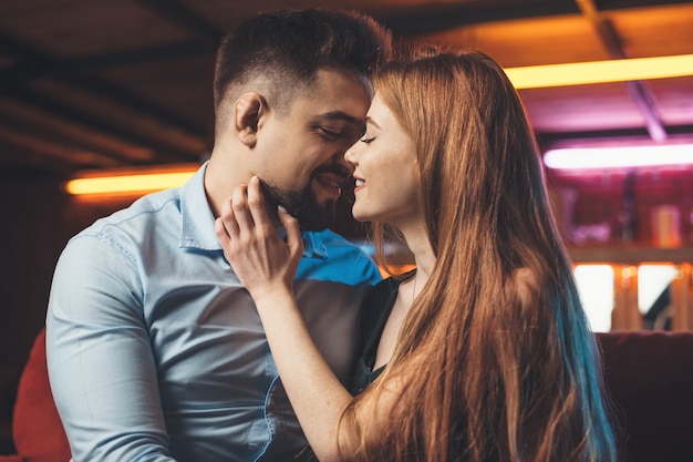 Close-up foto van een blanke gember vrouw omhelst haar minnaar en glimlach zittend op een bank