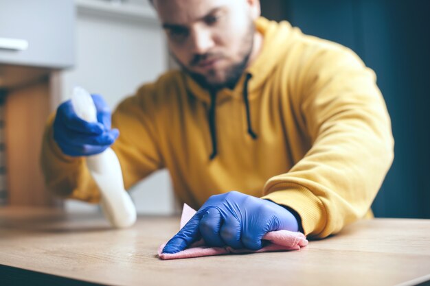 Close-up foto van een geconcentreerde man die de tafel schoonmaakt met een doekje en desinfecterende spray