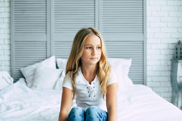 Close-up foto van een klein droevig blond meisje zit op haar bed in de kamer