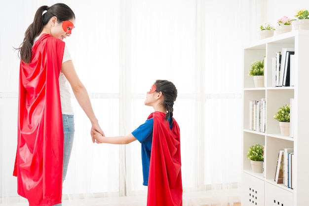 close-up foto van een lachende vrouw met een lief klein meisje dat naar elkaar kijkt en samen als superheld thuis speelt in de zomervakantie.