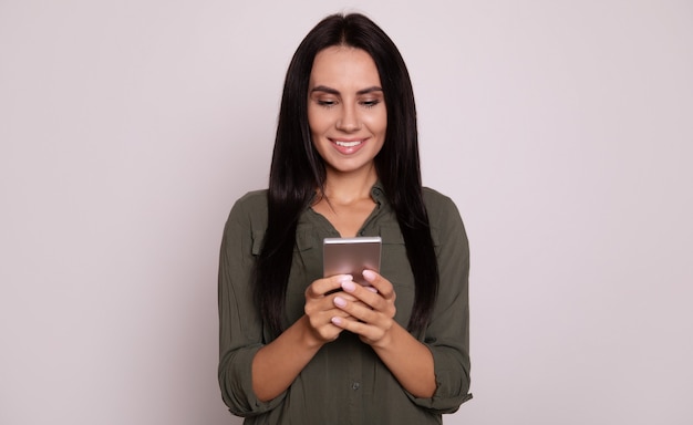 Close-up foto van een modern meisje met lang gitzwart haar houdt een smartphone in haar handen, glimlachend terwijl ze op internet surft of feed controleert