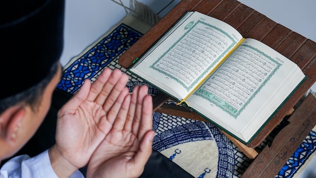 Foto close-up foto van een moslimman die de koran leest op een gebedsmat tijdens de heilige maand ramadan