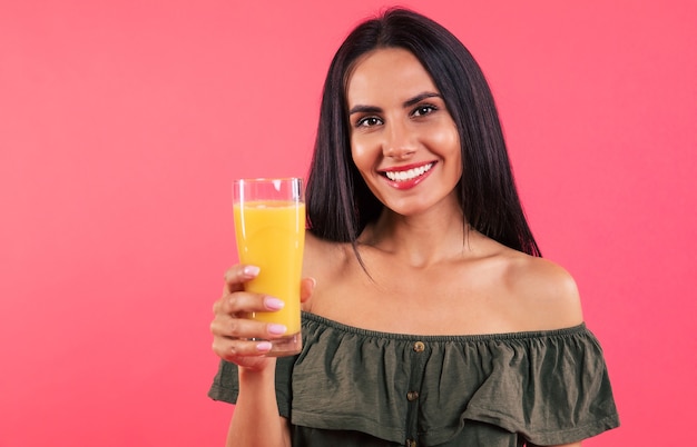 Close-up foto van een prachtige vrouw in een groene off-shoulder jurk, die een glas sinaasappelsap in haar rechterhand houdt en breed glimlacht