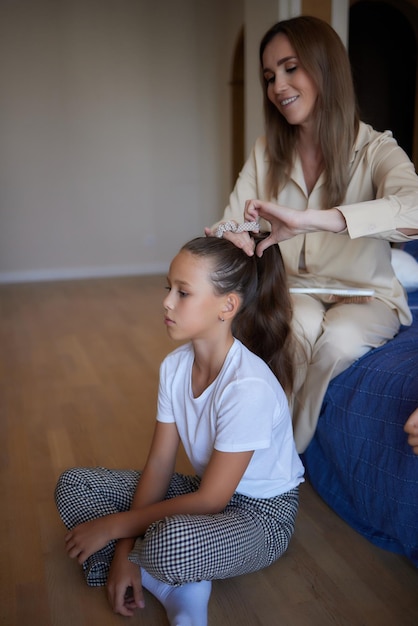 Close-up foto van gelukkig lachend schoolmeisje met krullend lang donker haar en haar mooie moeder die haar haar borstelt