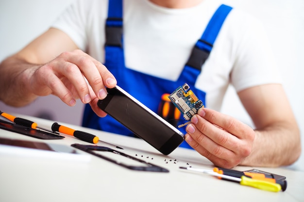 Close-up foto van gespecialiseerde man terwijl hij kapotte smartphone op zijn werkplek repareert met professioneel gereedschap