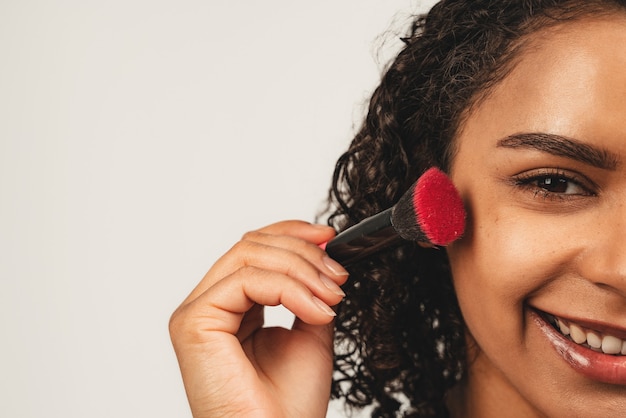 Close-up foto van gezicht aantrekkelijke zwarte vrouw houdt gezichtsborstel. GeÃƒ Â¯ Soleerd Op Witte Achtergrond.