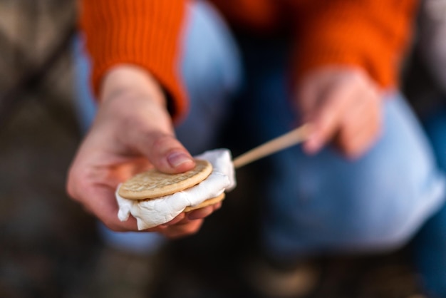 Close-up foto van het roosteren van marshmallows boven het vuur in de buurt van op de camping. Focus op vrouwelijke handen met stok en marshmallow erop. Jonge toerist die plezier heeft bij het vuur in de natuur