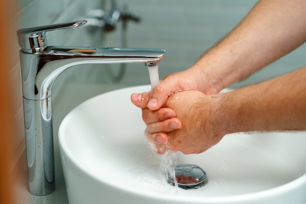 Close-up foto van mannelijke handen wassen met zeep boven de gootsteen binnenshuis