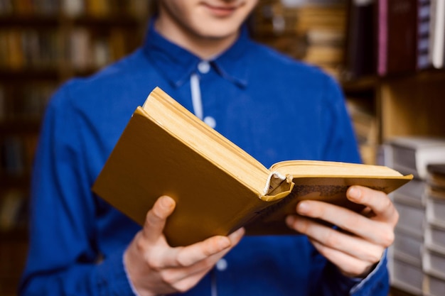 Close-up foto van mannelijke student met een boek in zijn handen die in de bibliotheek staat