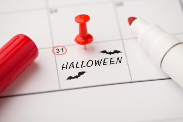 Close-up foto van markering op kalender op eenendertigste inscriptie halloween en vleermuizen tekenen met rode punaise en viltstift