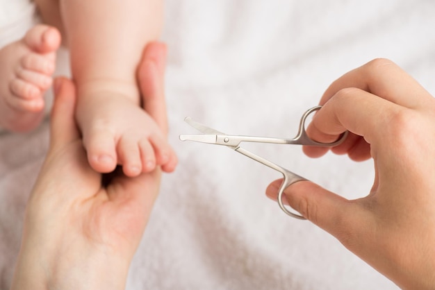 Close-up foto van moeders handen met pasgeboren voeten en baby nagelschaartje op geïsoleerde witte deken achtergrond