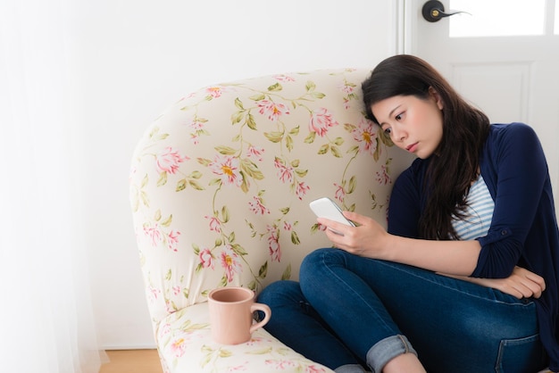 close-up foto van schoonheid lieve vrouw kijken naar mobiele smartphone verdriet voelen en zittend op een fauteuil wachten op bericht.