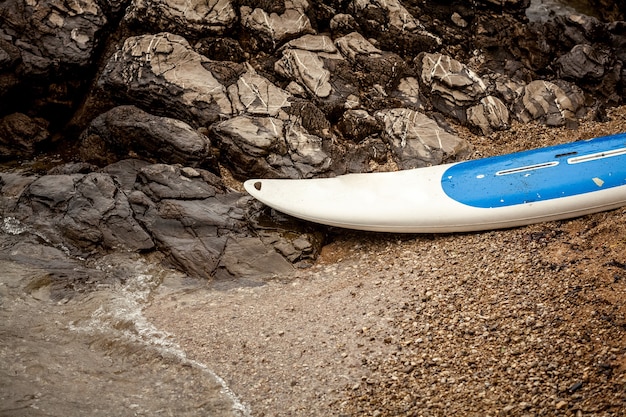 Close-up foto van surfplank liggend op zandstrand op zee naast grillige kliffen