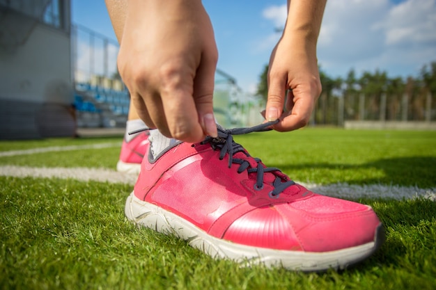 Close-up foto van vrouw die roze sneakers op voetbalveld vastbindt