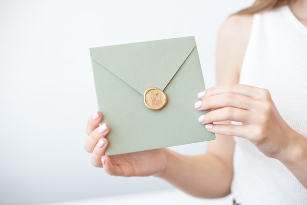 Close-up foto van vrouwelijke handen met een zilveren blauwe of roze uitnodigingsenvelop met een lakzegel, een cadeaubon, een briefkaart, een bruiloft uitnodigingskaart.