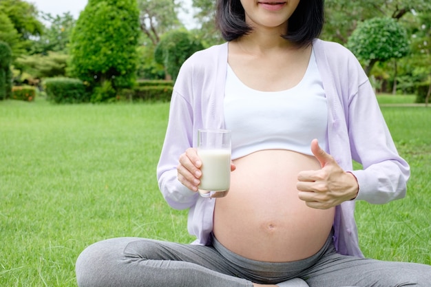 Close-up foto van zwangere moeder die zit en een glas melk vasthoudt om te drinken voor een goede gezondheid en duim omhoog