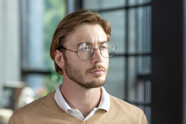 Close-up fotoportret van een jonge blonde man met een bril die serieus naar de kant kijkt die in een