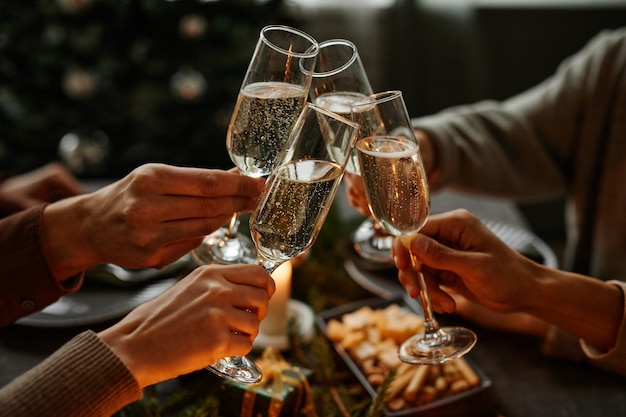 Close up of four people enjoying christmas dinner together and toasting with champagne glasses while...