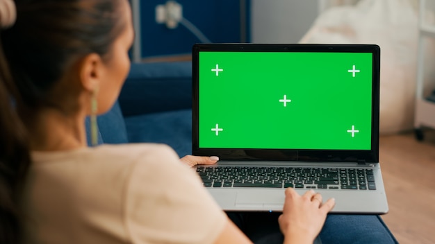 Close up of freelencer using laptop computer with mock up green screen chroma key display while sitting on sofa in living room., Woman working on personal business using isolated pc