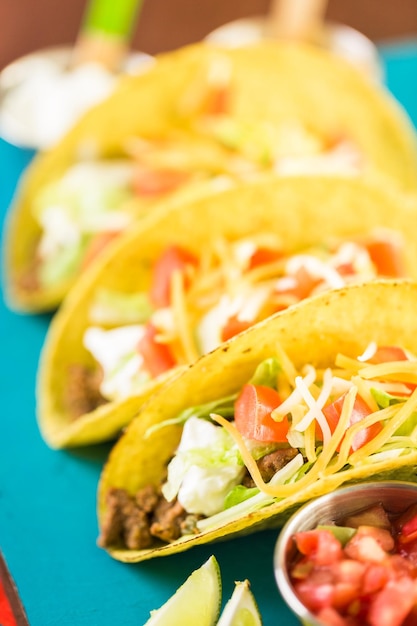 Close up of fresh beef tacos in hard yellow corn taco shell with sour cream and shredded cheese.