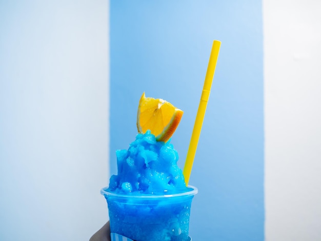 Close up fresh blue lemon smoothie with sliced yellow lime and yellow drinking straw in plastic cup