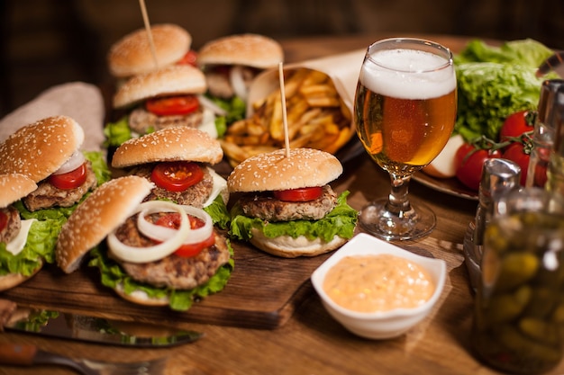 Close up of fresh burgers with a glass of beer on vintage wooden table. Delicious meat. Tasty pickles. Fresh bread. Great beer.