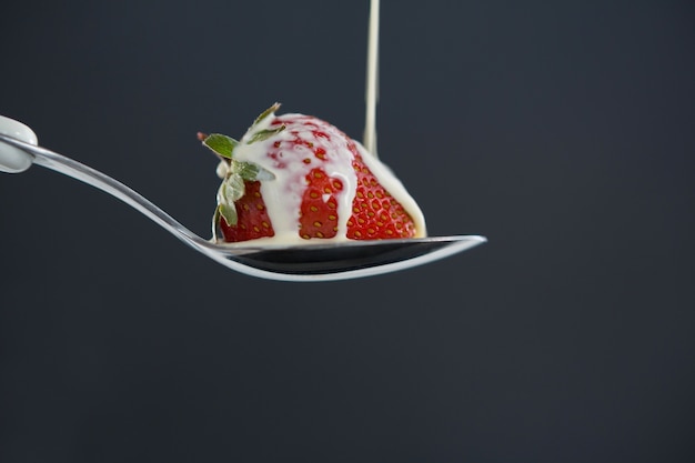 Close-up of fresh cream falling on spoon of strawberry against grey background