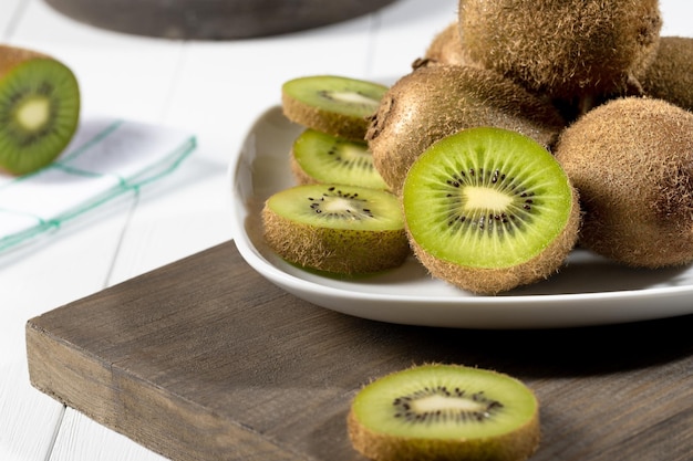 Photo close up fresh kiwi and slices on white plate on white wooden background selective focus