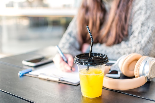 Student39 の机の上に蓋とストローが付いたプラスチック カップに入った新鮮なオレンジ ジュースの接写