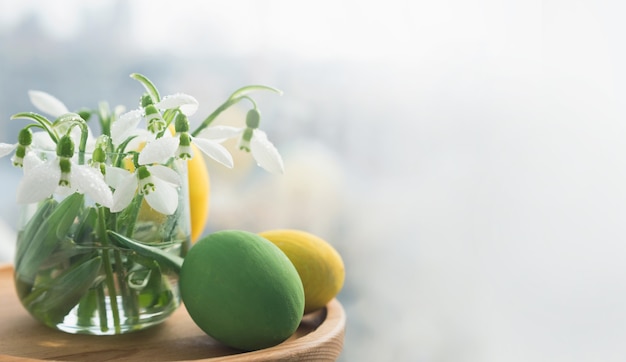 Close up fresh snowdrops in a glass vase and easter eggs. Banner with copy space