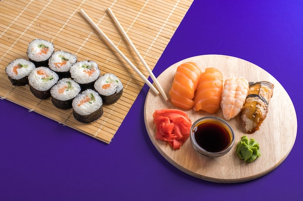 Close up of fresh sushi and rolls served on wooden board and bamboo mat.