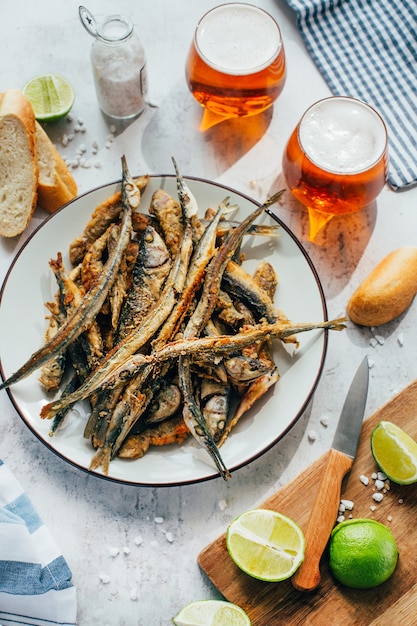 Close-up of fried fish anchovy in a plate next to beer in glasses and lime on a board