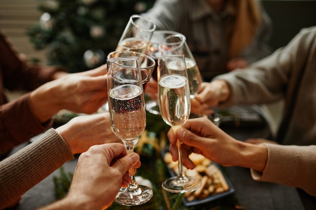 Close up of friends clinking champagne glasses while enjoying christmas dinner together sitting by e...