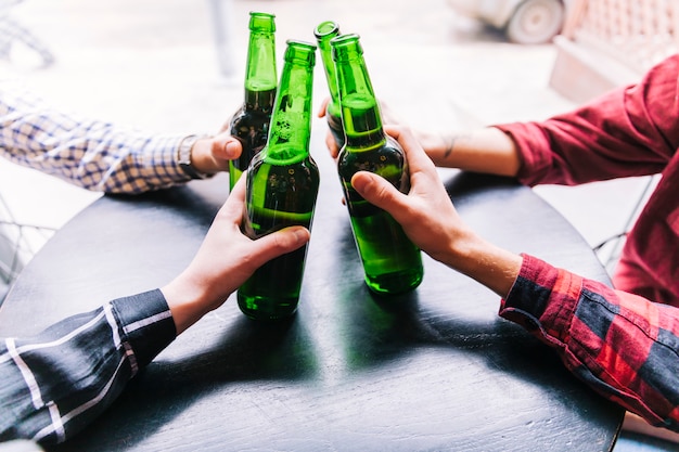 Photo close-up of friends holding the beer bottles over the wooden table