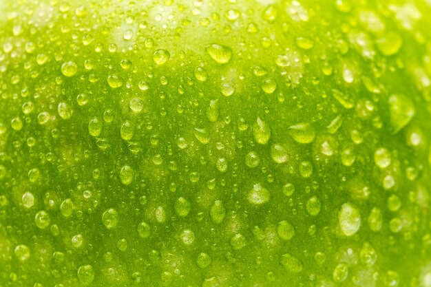 Un primo piano da una mela verde con gocce d'acqua come texture di sfondo. scattata in studio con una 5d mark iii.