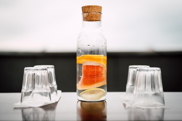 Photo close-up of fruit slices in drink jar amidst shot glasses on table