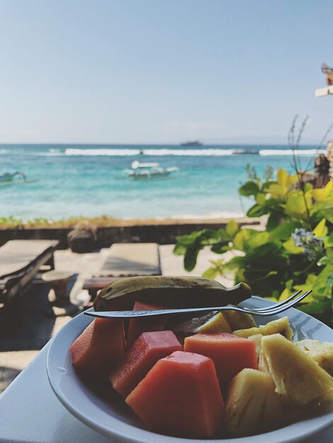 Photo close-up of fruits in bowl against beach