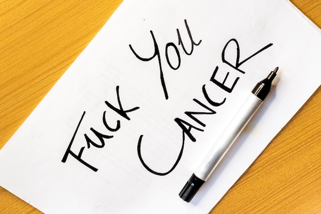 Close up of Fuck Cancer message handwritten on a sheet of paper with a black marker pen Fight against cancer overcoming illness problems health