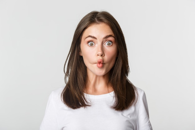 Close-up of funny and cute brunette girl suckink lips, making fish grimace, white.