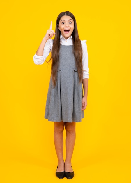 Close up funny face of young teenager pointing up with finger isolated on yellow background Girl has