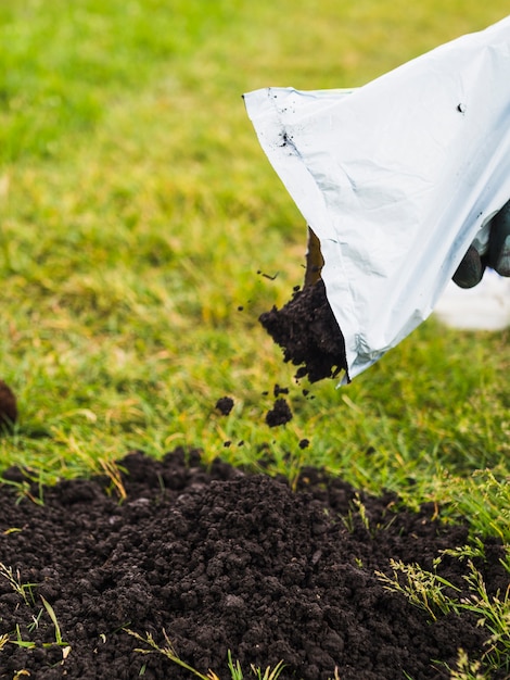 Photo close-up of gardener pouring soil from hand on lawn