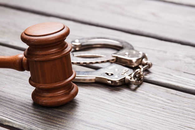 Close-up gavel and handcuffs. Wooden hammer and metal handcuffs on the desk.