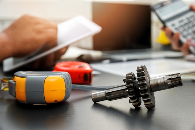 Photo close-up of gear and measure tape with people working in background on table