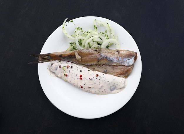 Close-up gedeelte van gezouten ingelegde haring visfilets met uien en saus op witte plaat over zwarte tafel, verhoogde bovenaanzicht, direct boven