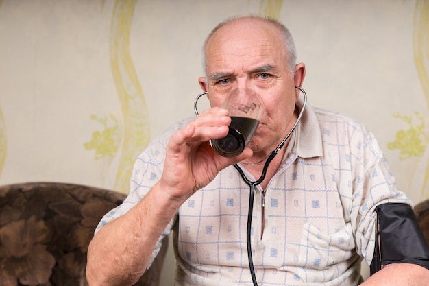 Close-up gehandicapte oudere man met stethoscoop, een glas gezond sap drinkend terwijl hij serieus naar de camera kijkt