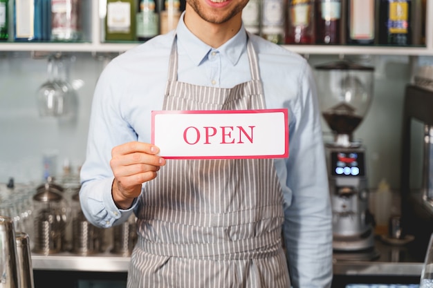 Close up of gentleman demonstrating signboard with word open and inviting to visit his cafe